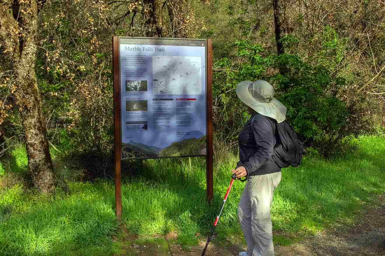 A woman looking at a sign in the woods.