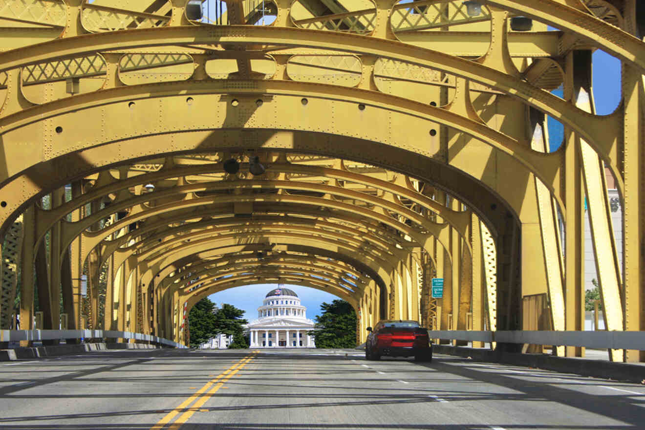 A car is driving under a yellow bridge.