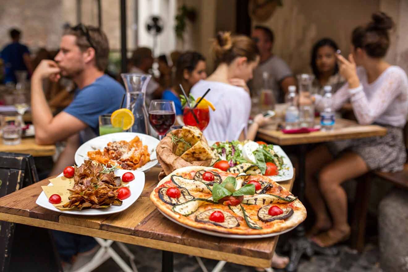 table with italian food with a group of people sitting at the tables in the background