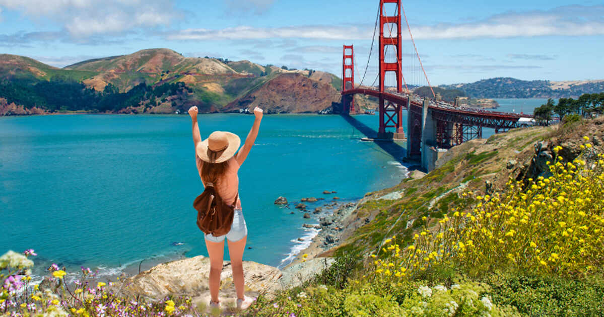 A woman is standing on top of a hill overlooking the golden gate bridge.