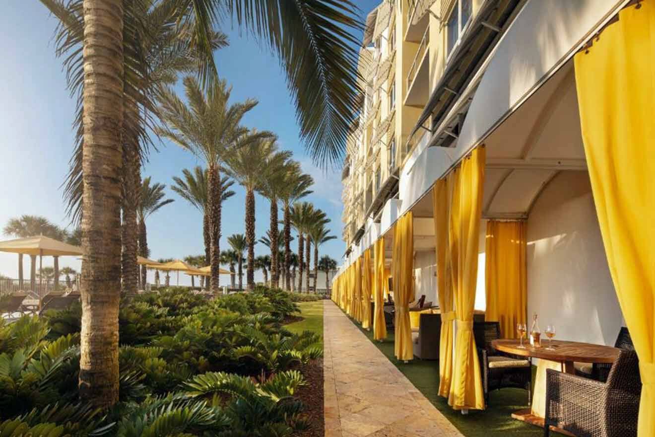 A walkway with yellow curtains and palm trees.