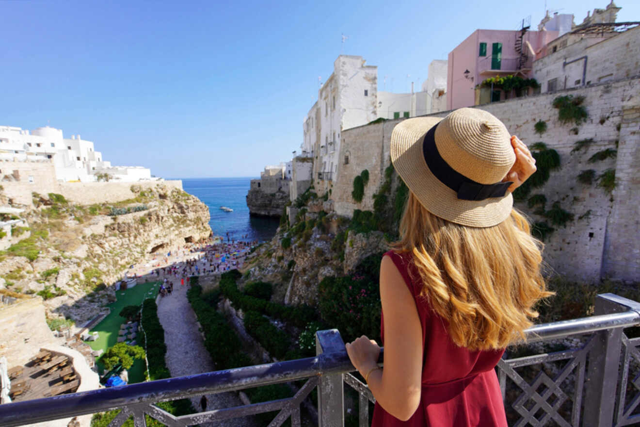 A woman in hat is standing on a balcony overlooking the sea.