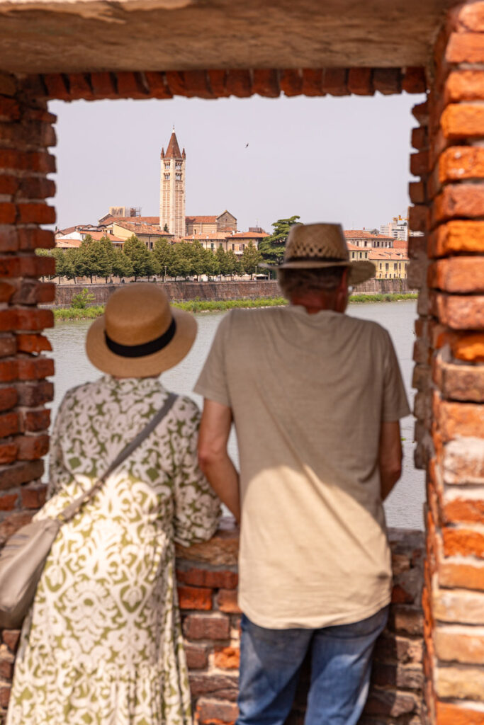 two people looking out brick window on bridge to church steeple on adige river