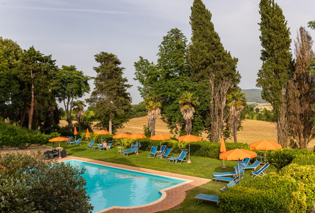 swimming pool surrounded by orange umbrellas and cypress trees