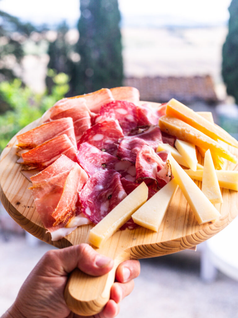 hand holden wooden board full of cured meat and cheeses