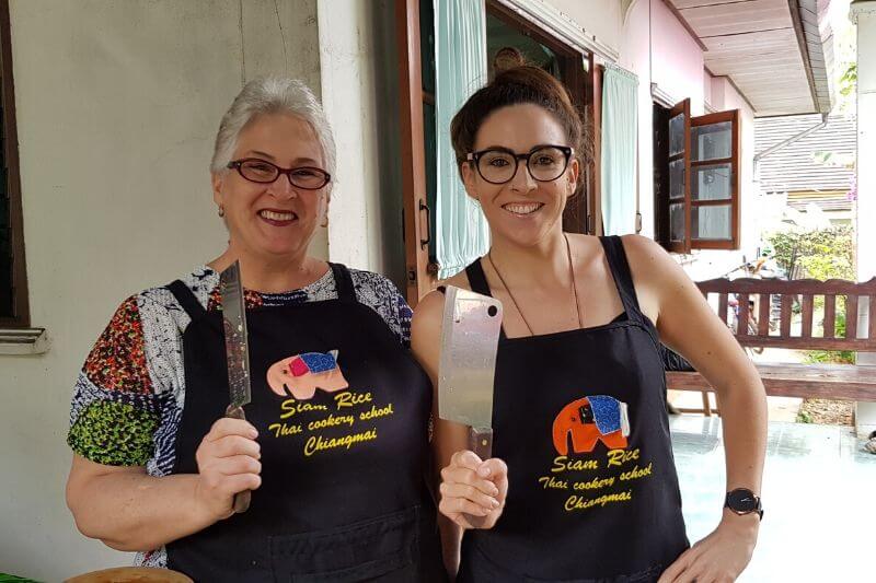 two peop;e holding knives up in thai cooking class