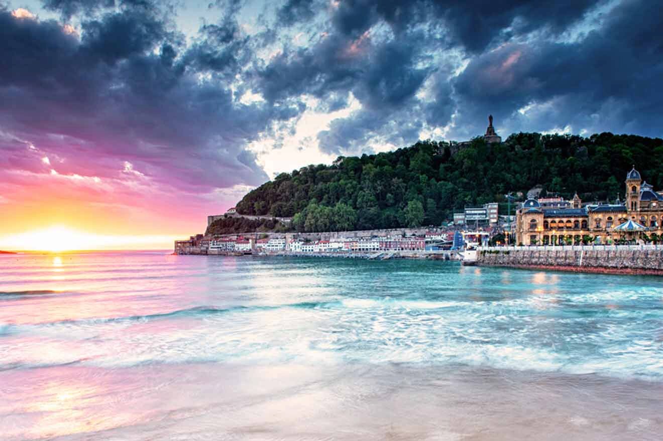 The sun is setting over a beach with buildings in the background.