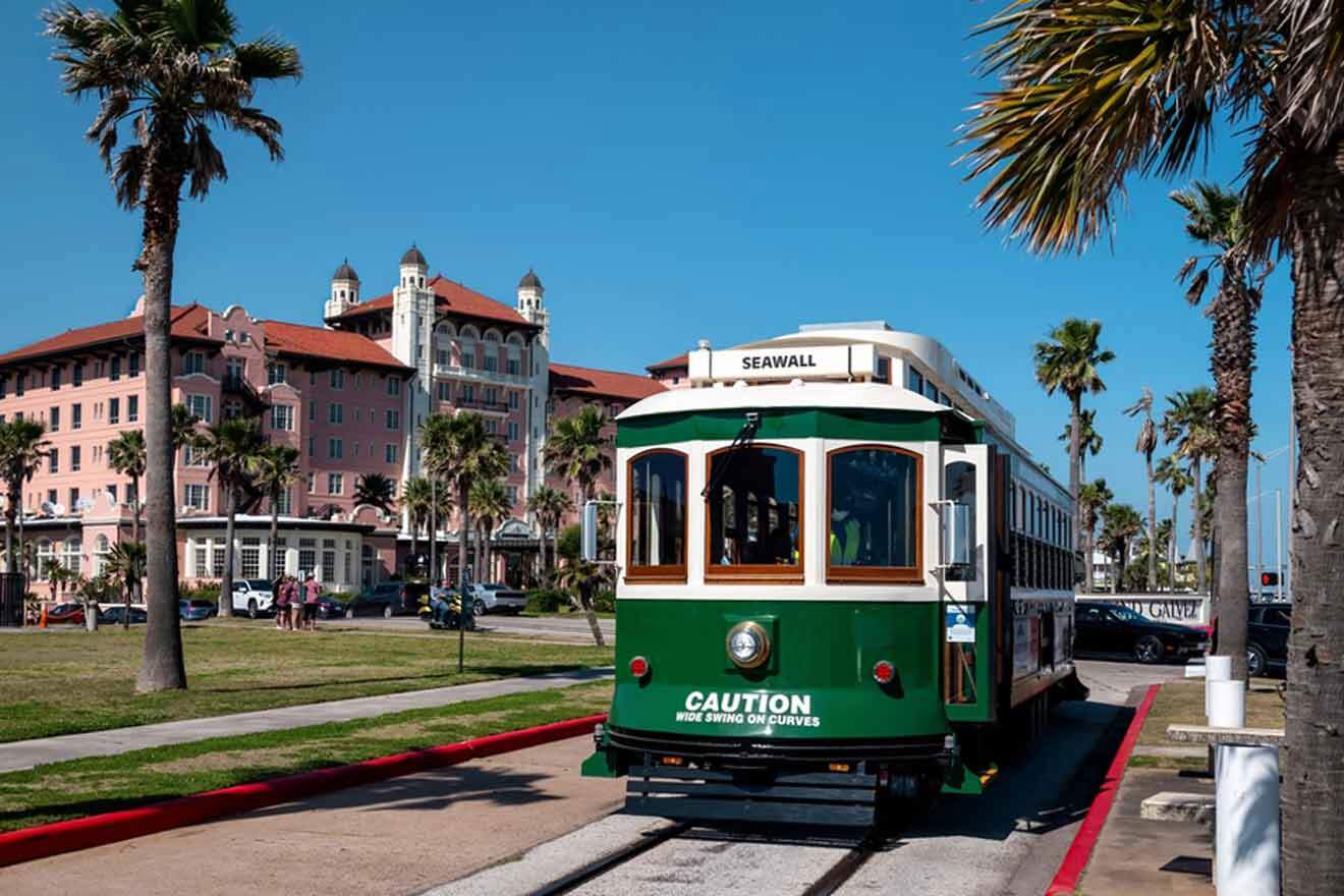 A green trolley is on the tracks in front of a building.