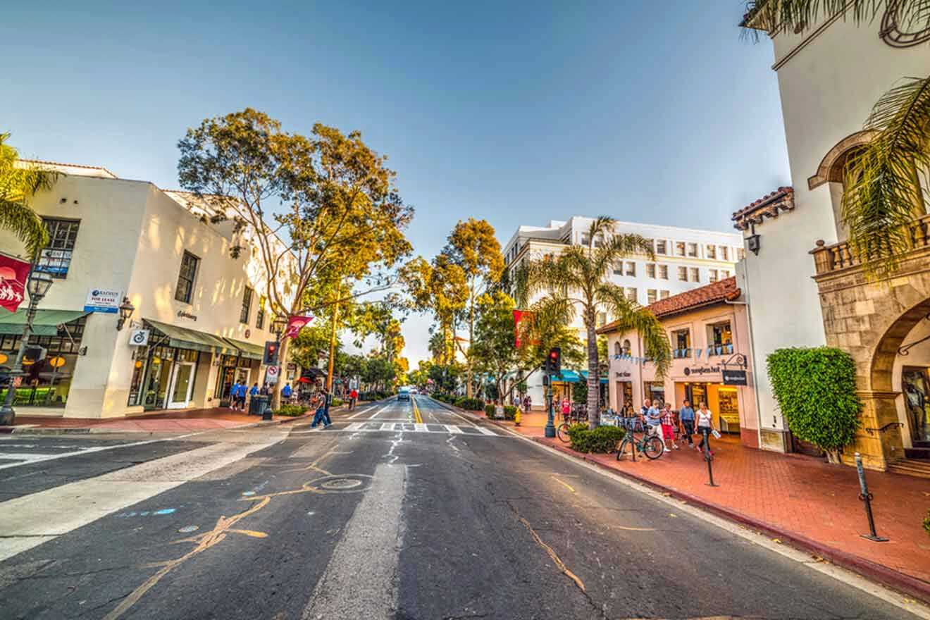 street with various shops with people walking on the sidewalk and tall trees