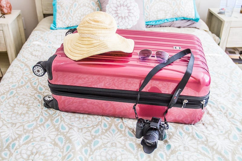 29" Delsey suitcase on bed with hat and camera