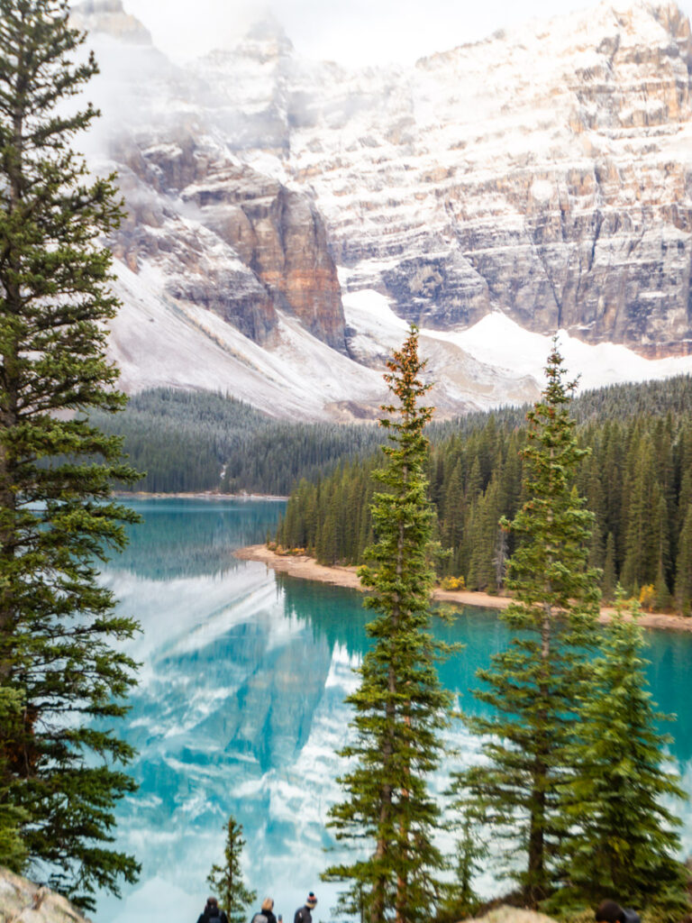 lake moraine framed by trees with snow covered mountains 