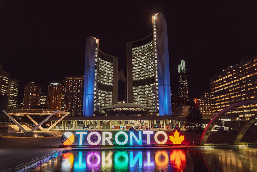 neon sign that says Toronto in front of buildings lit up at night