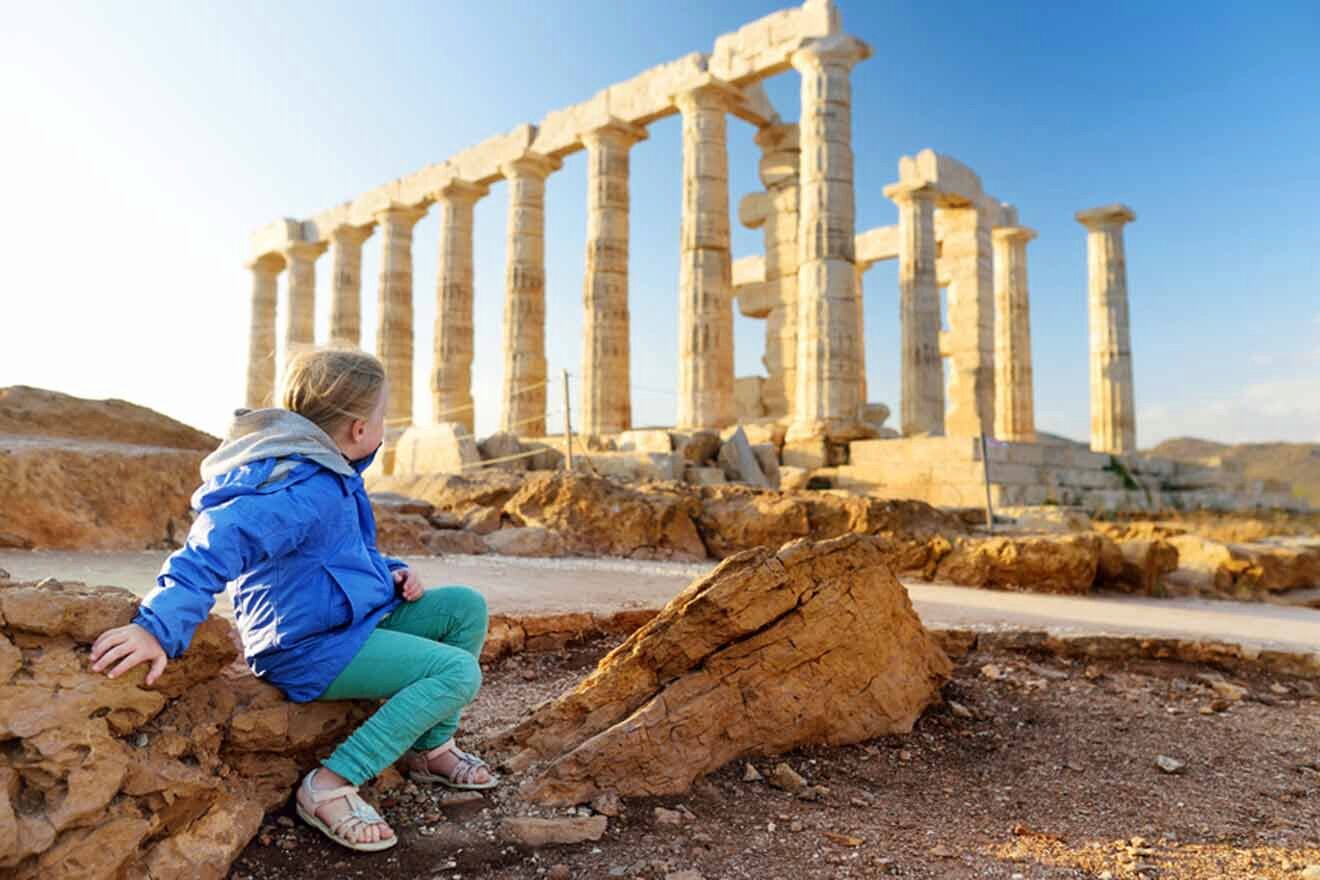 A little girl is sitting on a rock in front of a temple.