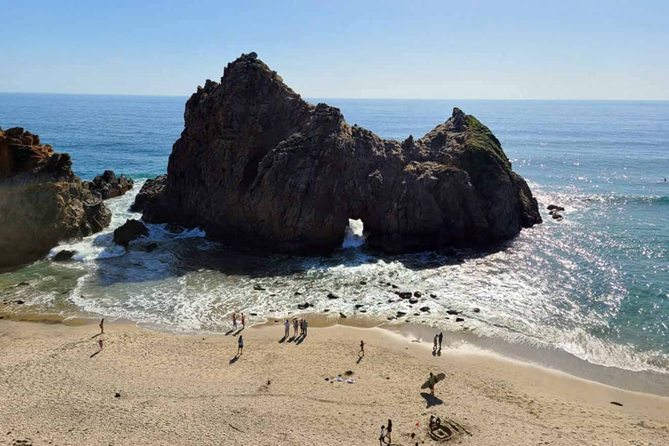 A group of people are standing on a beach near a rock formation.