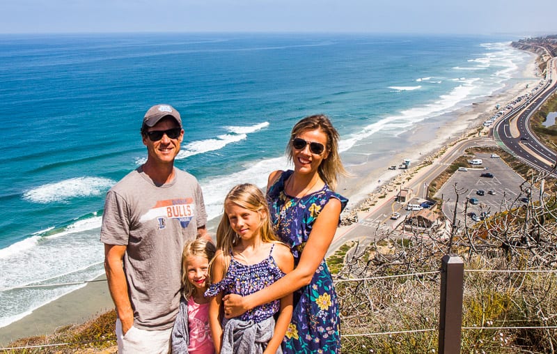 family posing on cliff top with pacific ocean views behind them at Torrey Pines State Natural Reserve