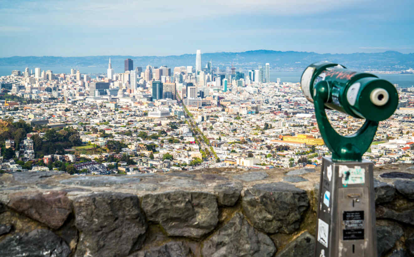 San Francisco's expansive cityscape viewed from Twin Peaks, with a coin-operated telescope in the foreground framing the urban expanse under a cloudy sky.