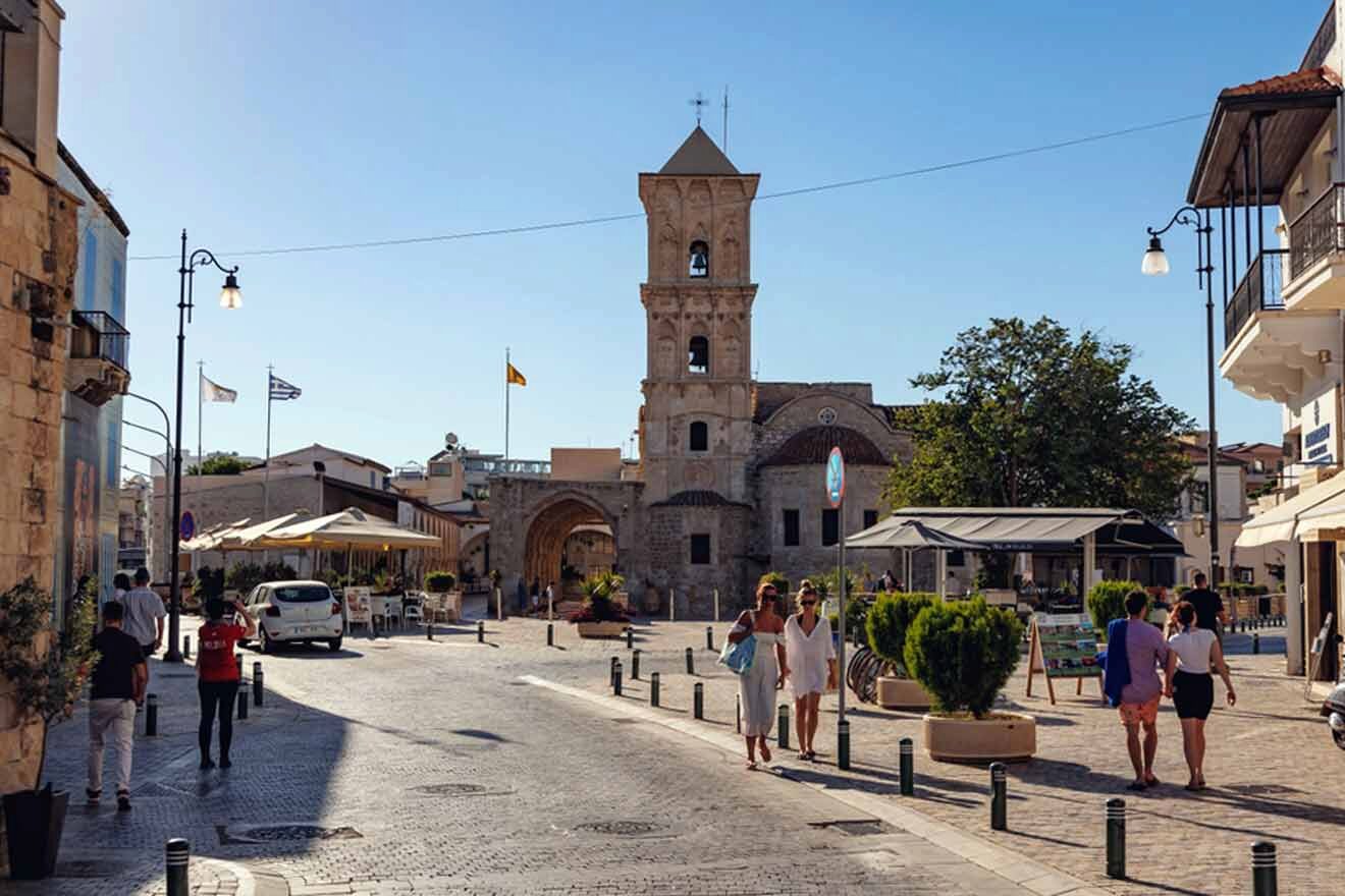 People walking down a street  in Larnaca with a church in the background.