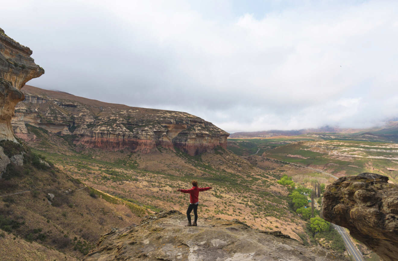 a woman holding out hands at a rock view point over a landscape