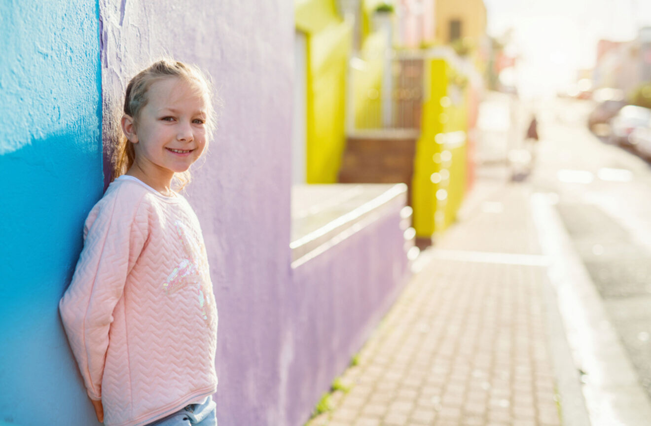 a girl leaning against a colorful house in a narrow street