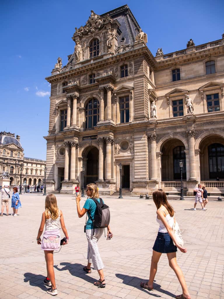 Mom and two daughters walking through a plaza in front of a historic building.