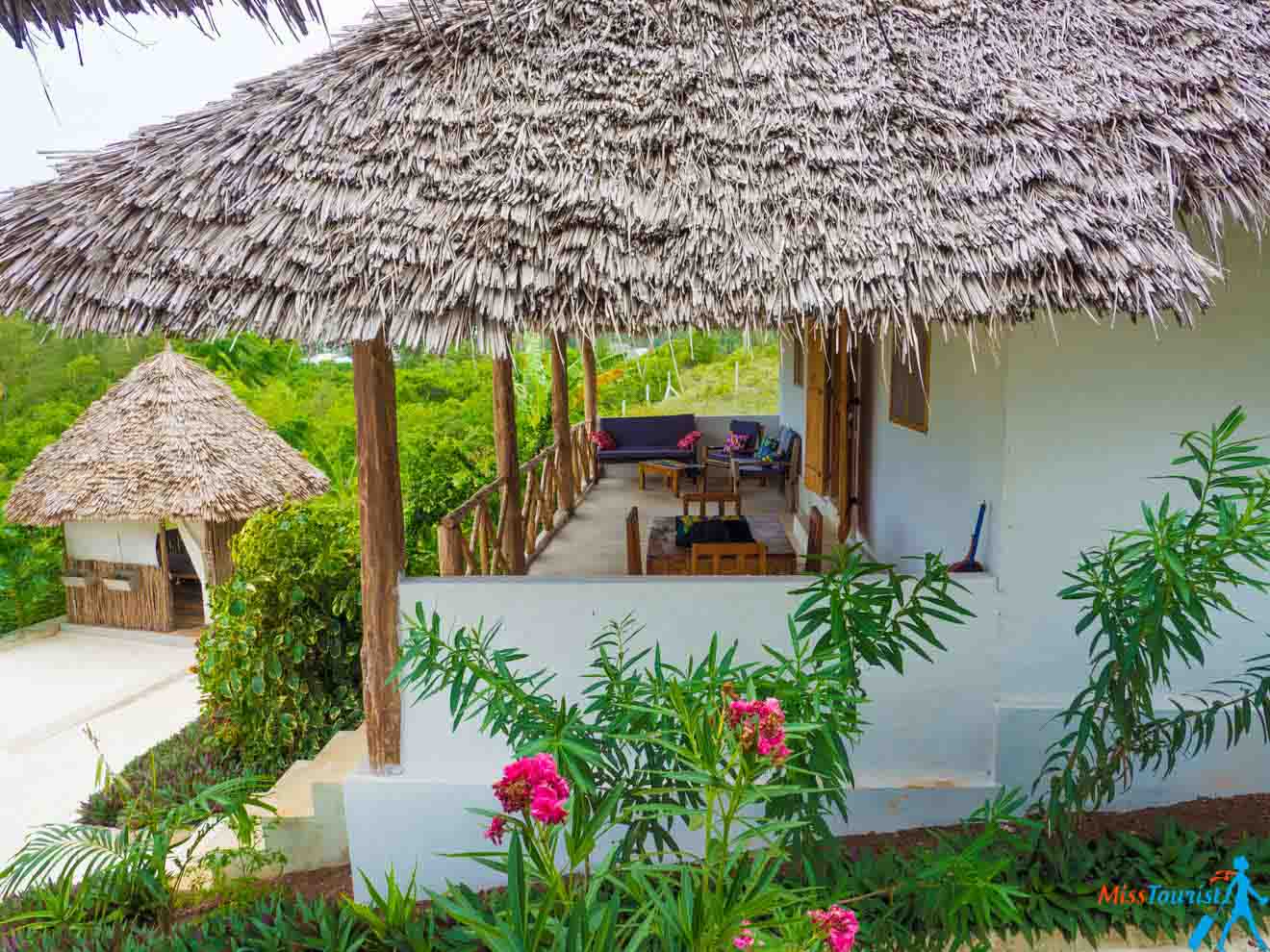 A hut with thatched roof and a balcony with sofas, armchairs, and chairs with a table