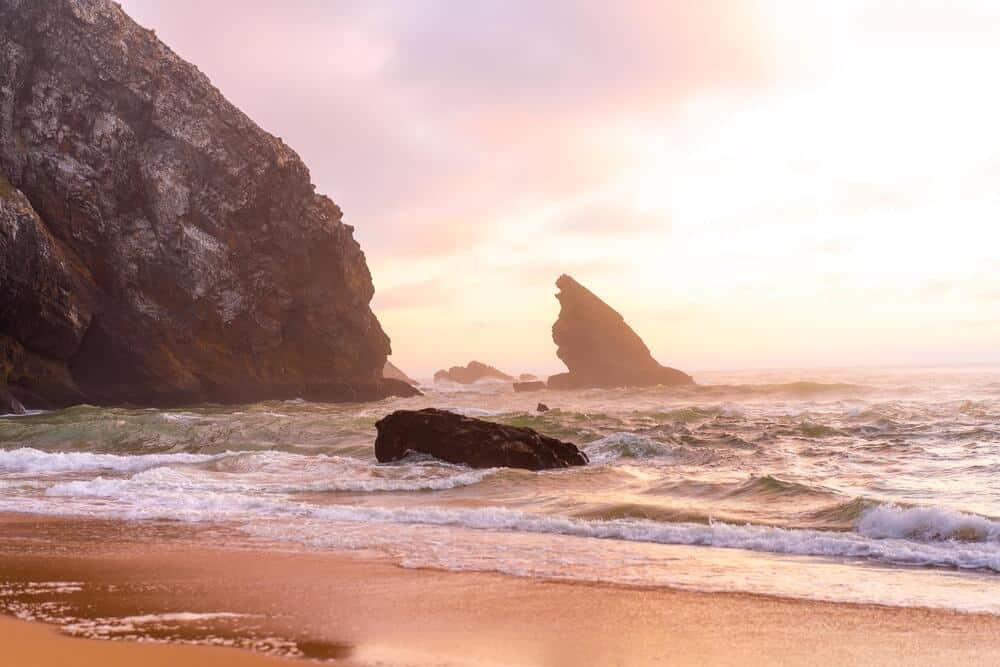 Sunset on the Ocean wild beach stormy weather. Praia da Adraga sandy beach with picturesque landscape background,