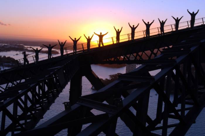 people standing on Sydney Harbour Bridge with arms in the air  at Twilight