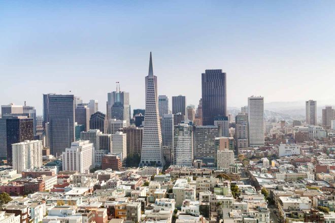 A daytime panorama of San Francisco's skyline, featuring the prominent Transamerica Pyramid among a dense collection of high-rise buildings under a clear sky