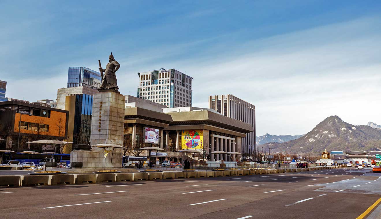 A street in Seoul with a statue in the middle of the road and mountains in the background