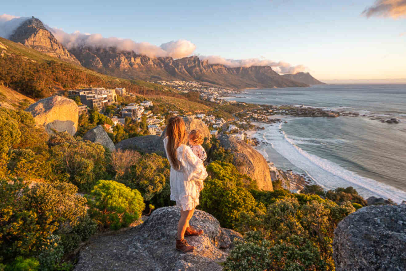 A woman holding a child standing on a rock overlooking a town on the coast