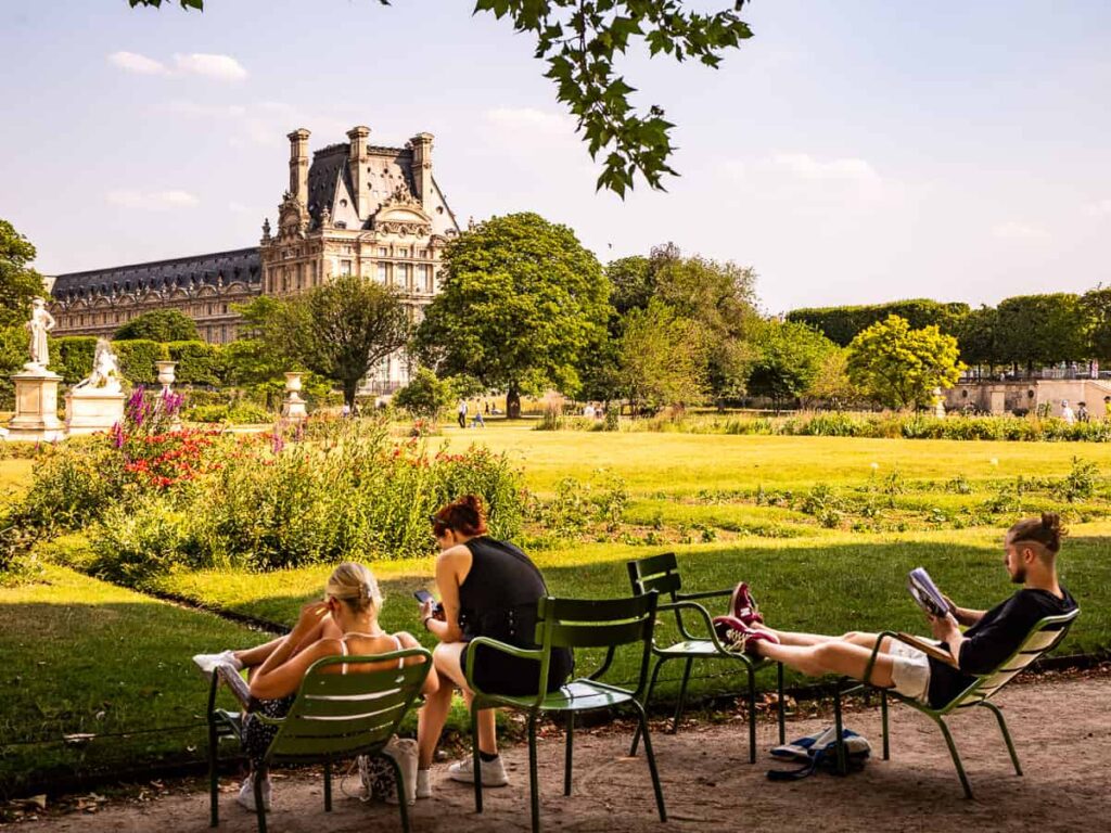 people sitting on chairs in Tuileries garden looking at louvre