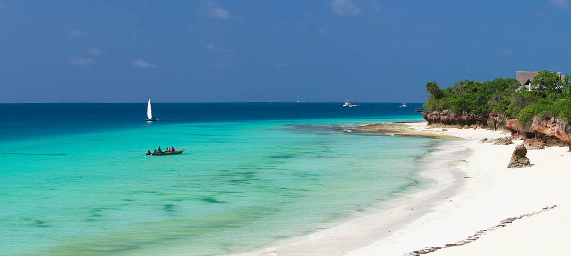 A white sand beach with cliffs and boats in the water in Zanzibar