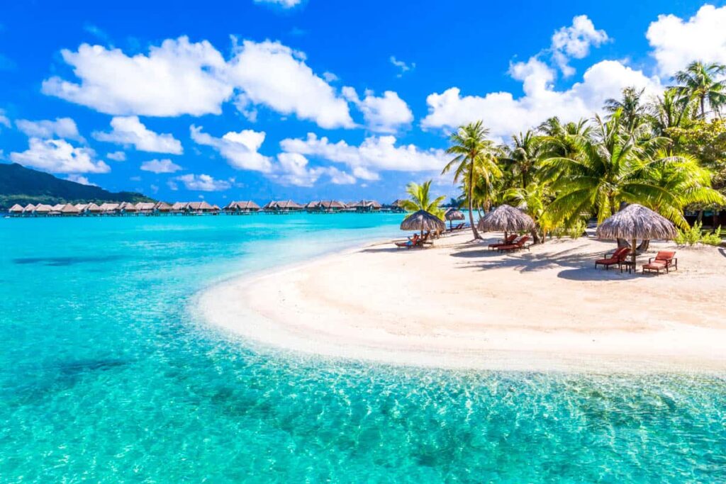 white sandy island with over water bungalows in background