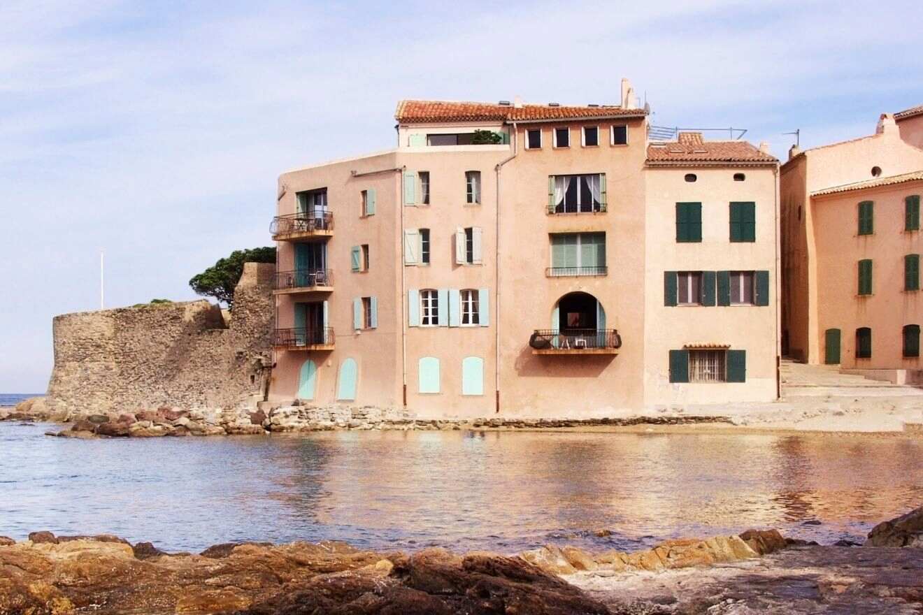 A vibrant view of the town of Saint-Tropez with terracotta-roofed buildings along the seafront, set against a backdrop of green hills and a clear blue sky