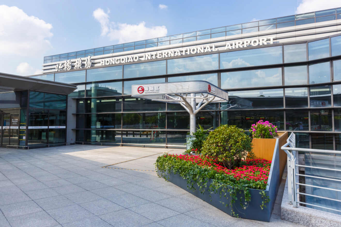 The entrance to Hongqiao International Airport in Shanghai, featuring a modern glass facade and a landscaped front area with bright flowers