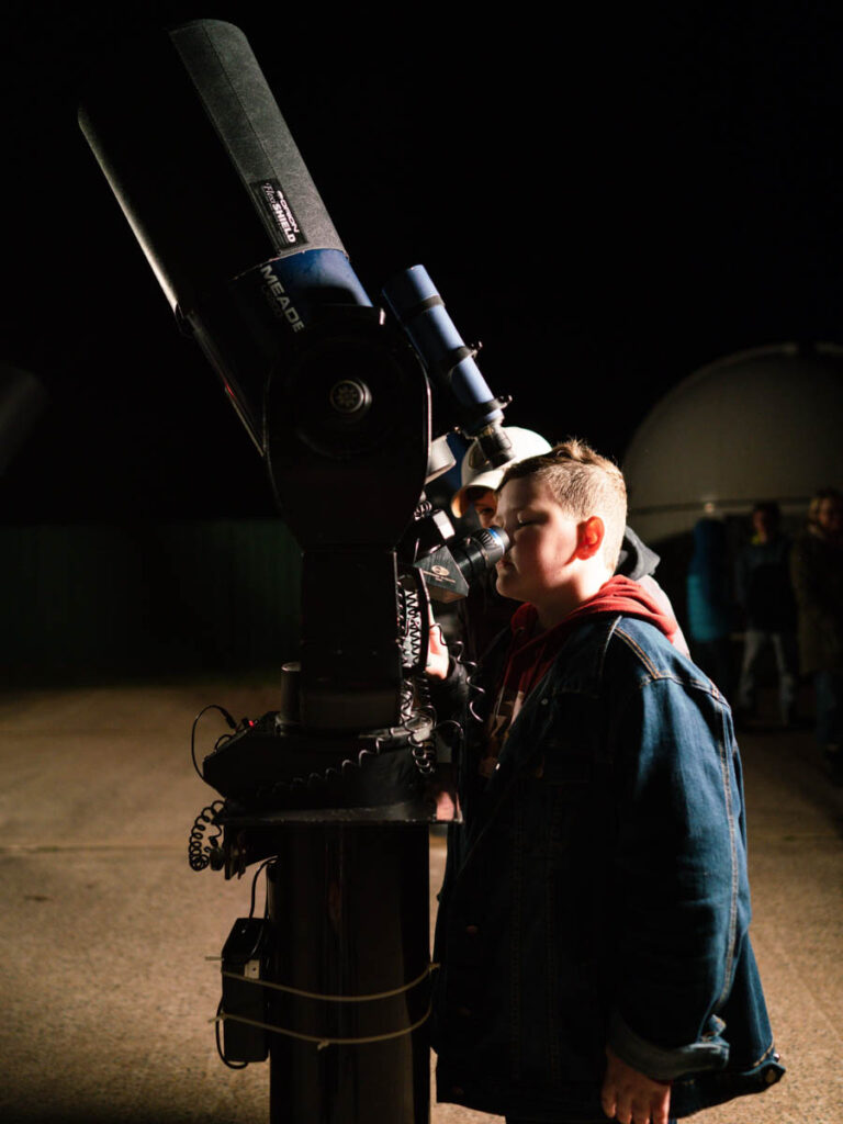 boy looking into telescope on roof of observatory