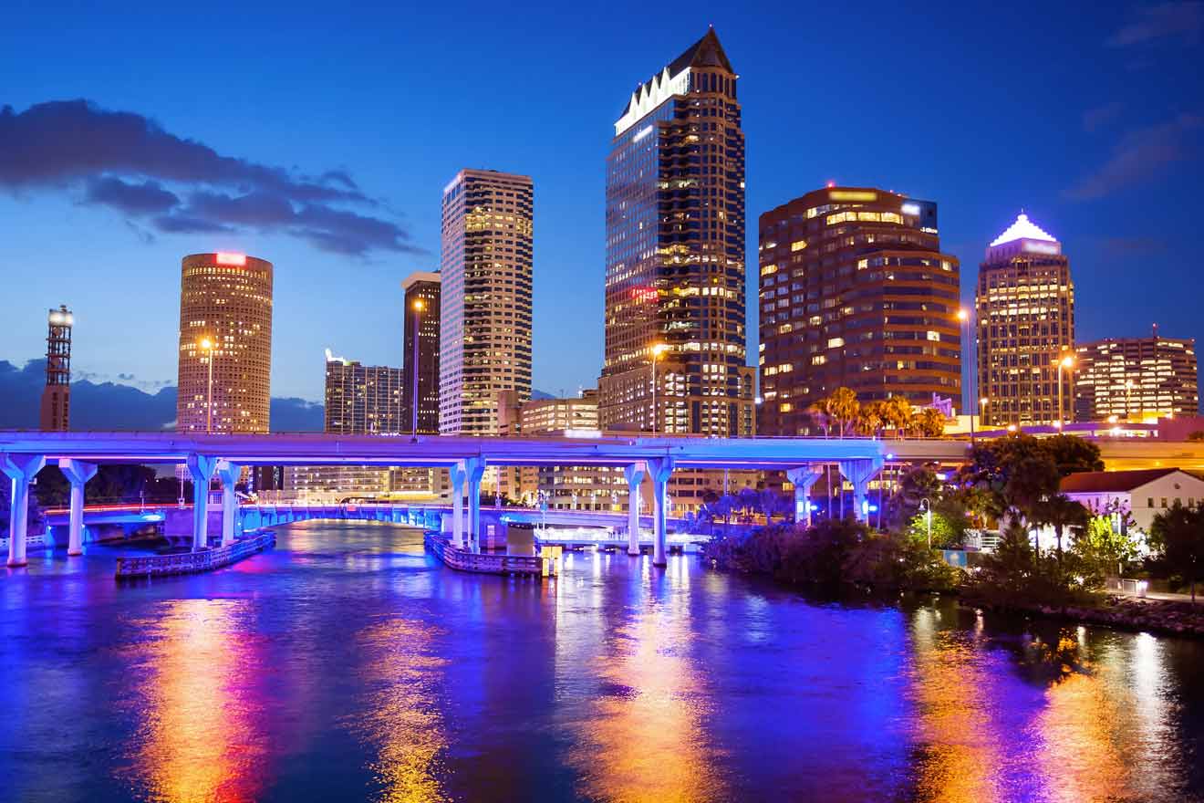 Evening view of Tampa's illuminated skyline with bridges over the river, reflecting colorful lights