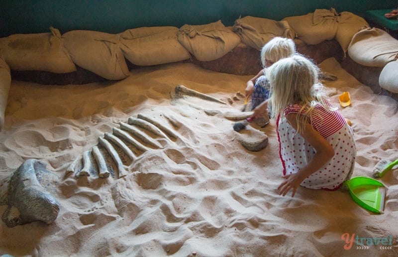 two young girls in sandpit digging dinosaur bones