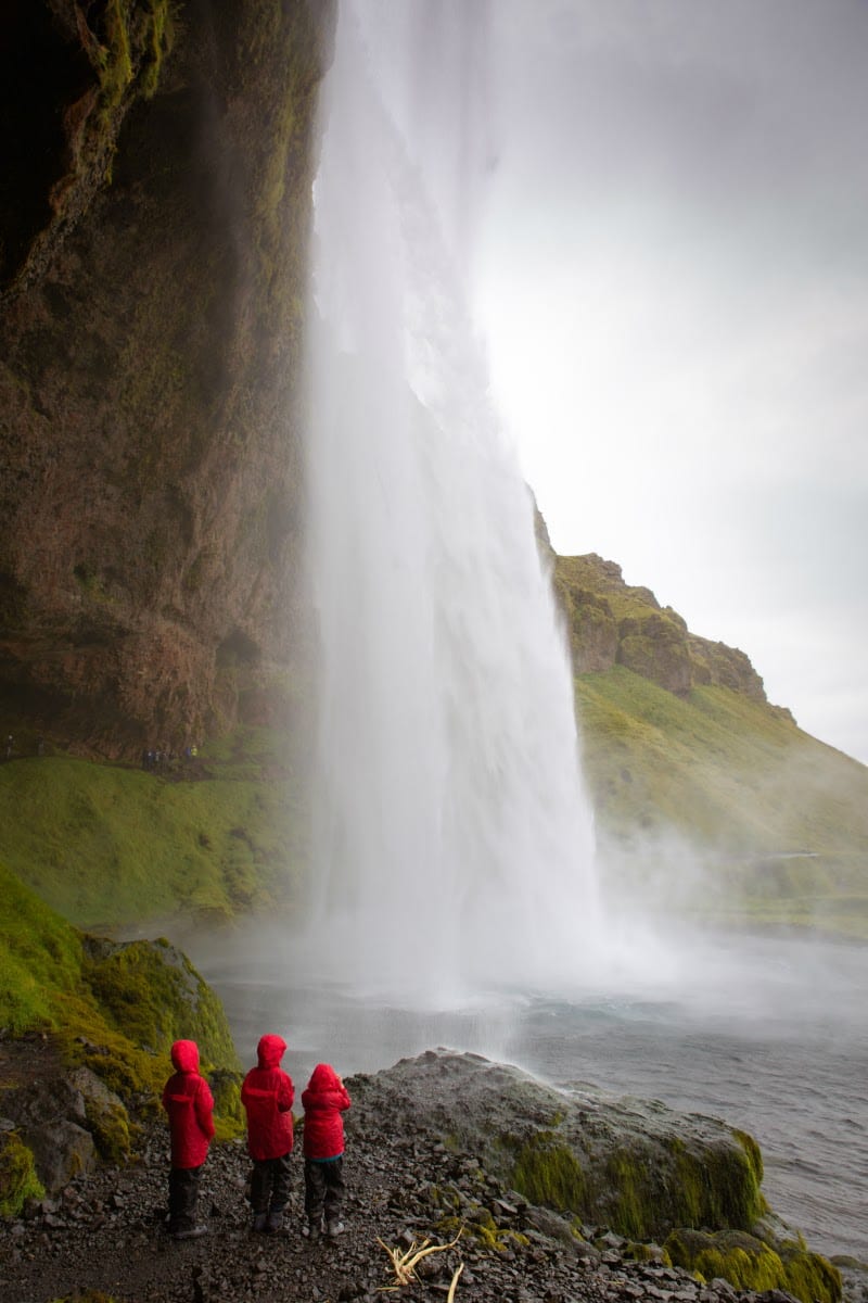 kids in red raincoats looking at Seljalandsfoss waterfall 