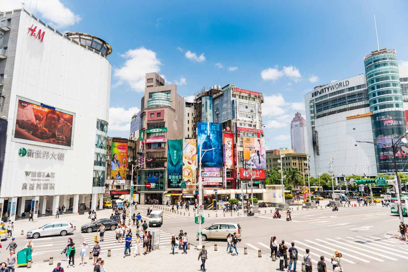 Busy intersection in Taipei with diverse advertising billboards and a bustling crowd of pedestrians