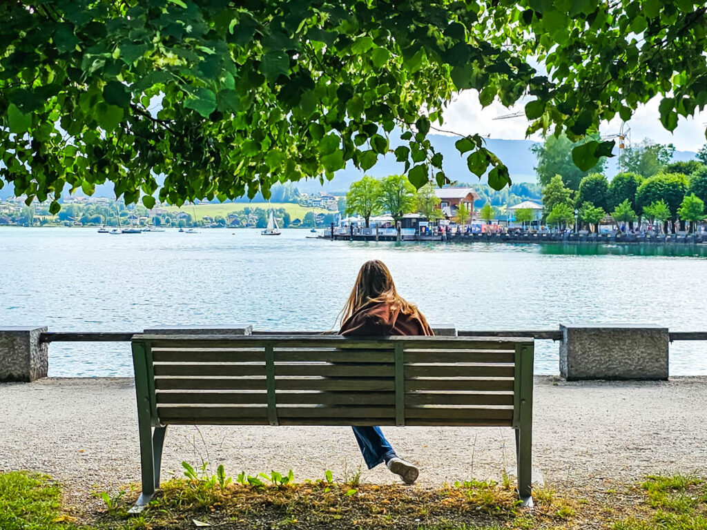 girl sitting on bench looking at view of lake