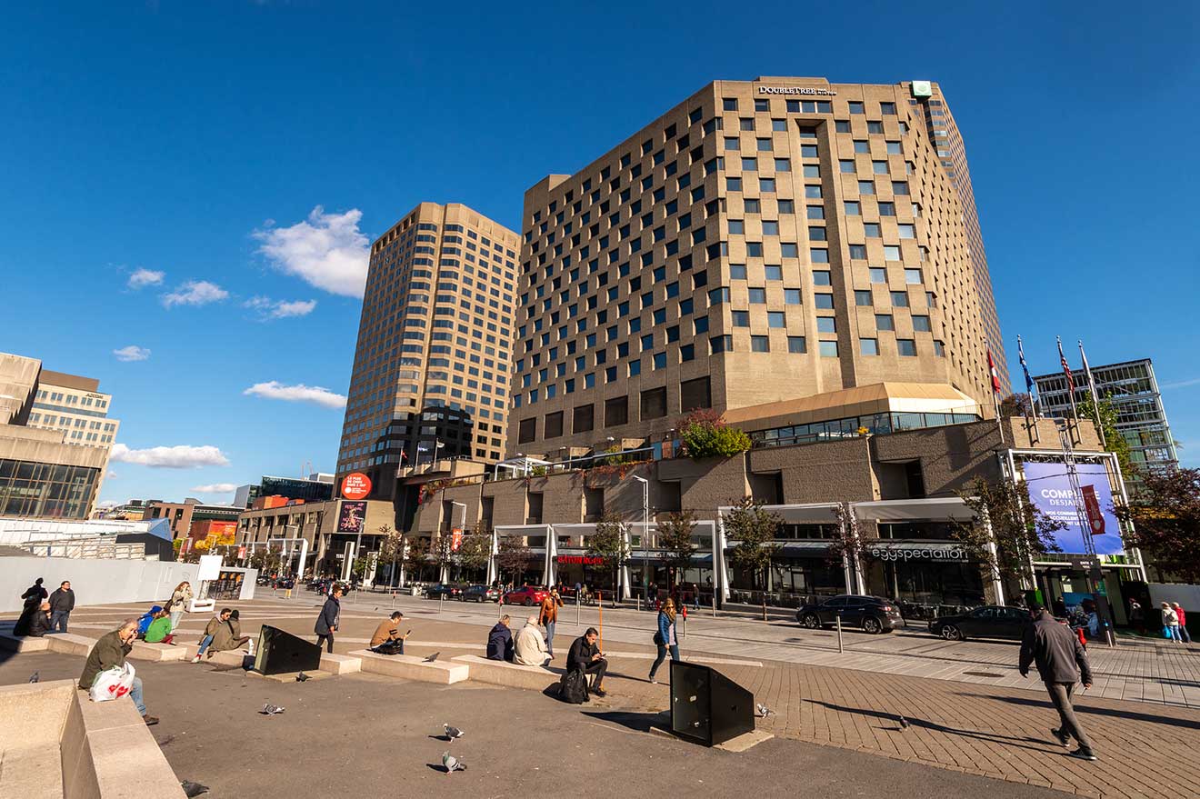 Daytime urban scene in Montreal with people lounging around a plaza, high-rise buildings, and a DoubleTree hotel dominating the skyline.