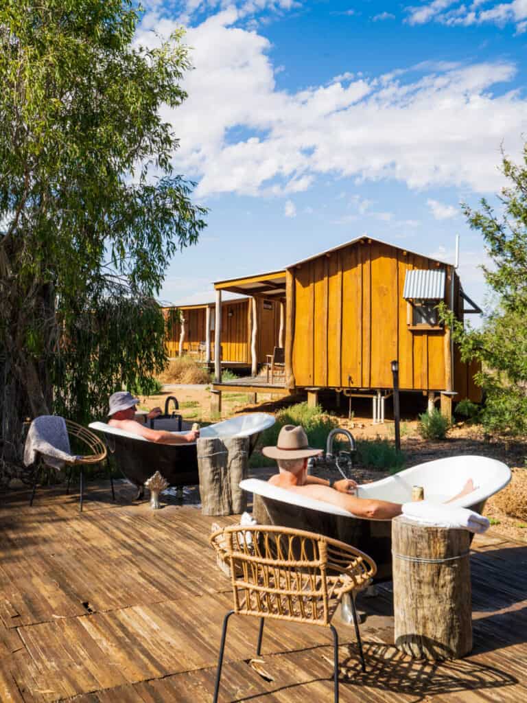 people sitting in bathtubs on deck near rustic cabins