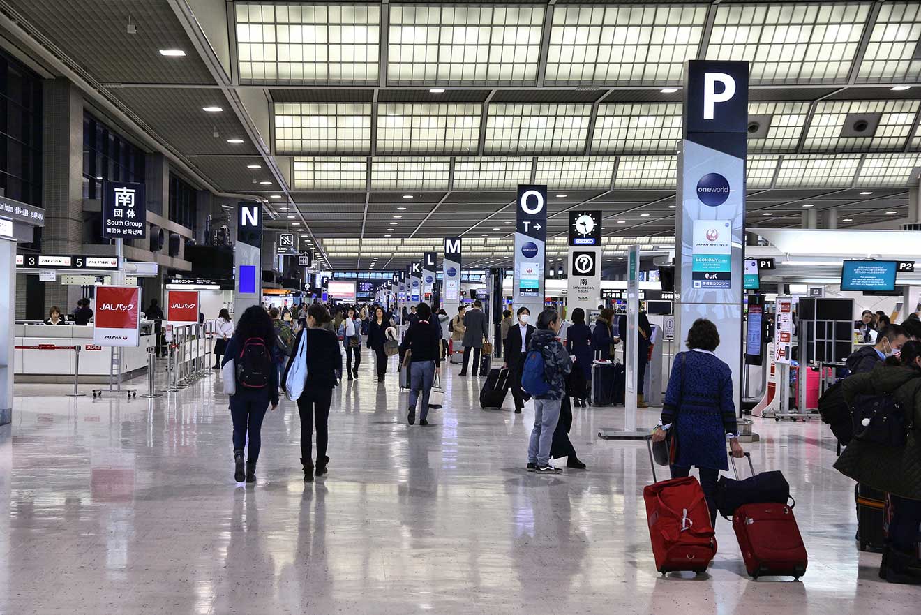 Busy terminal inside Narita International Airport with passengers and informational signage