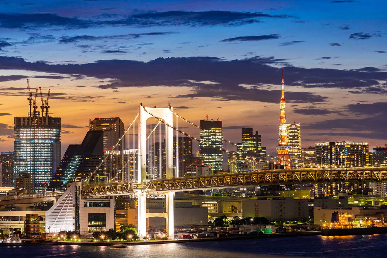 Twilight scene of Tokyo Bay with Rainbow Bridge and Tokyo Tower illuminated against the city's night skyline