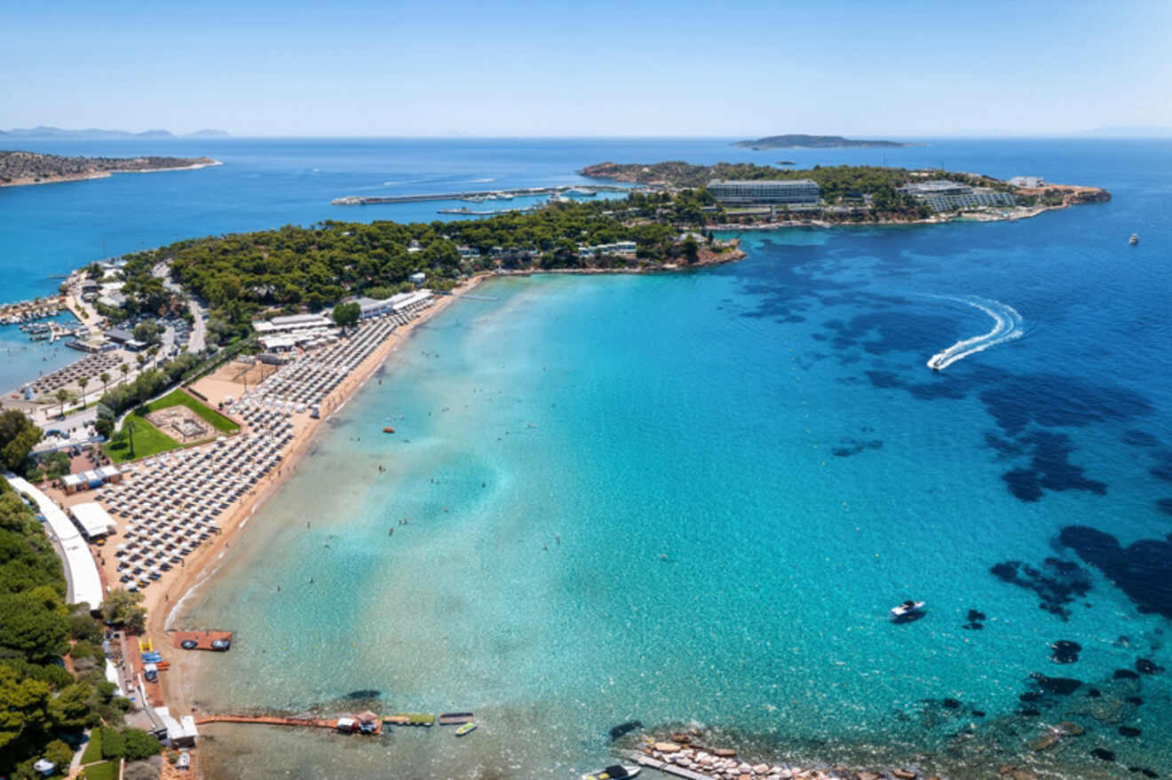 Overhead view of a peninsula in Athens showing clear turquoise waters, boats, and beachgoers, with resorts and greenery lining the shore