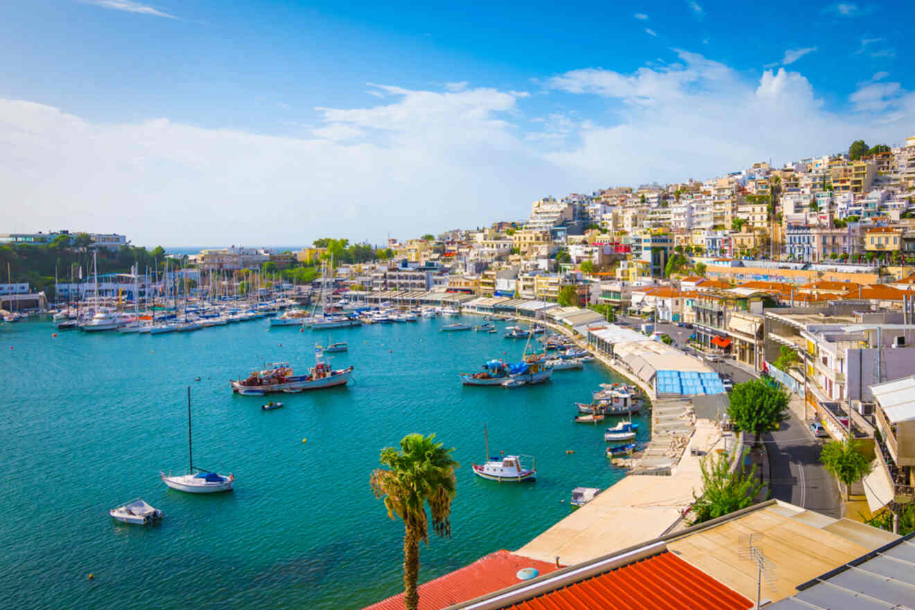 A vibrant marina in Athens with moored boats, surrounded by a densely packed hillside neighborhood and clear Mediterranean skies