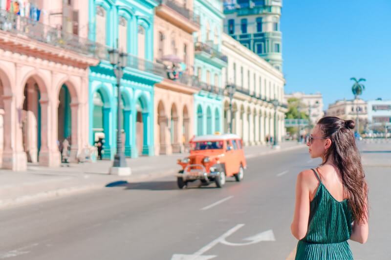 lady looking at old car drive past colorful buildings in havana cuba