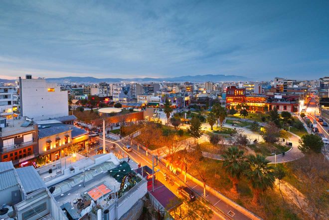 An evening scene of a vibrant Athens neighborhood with illuminated streets and buildings, highlighting the city's lively nightlife.