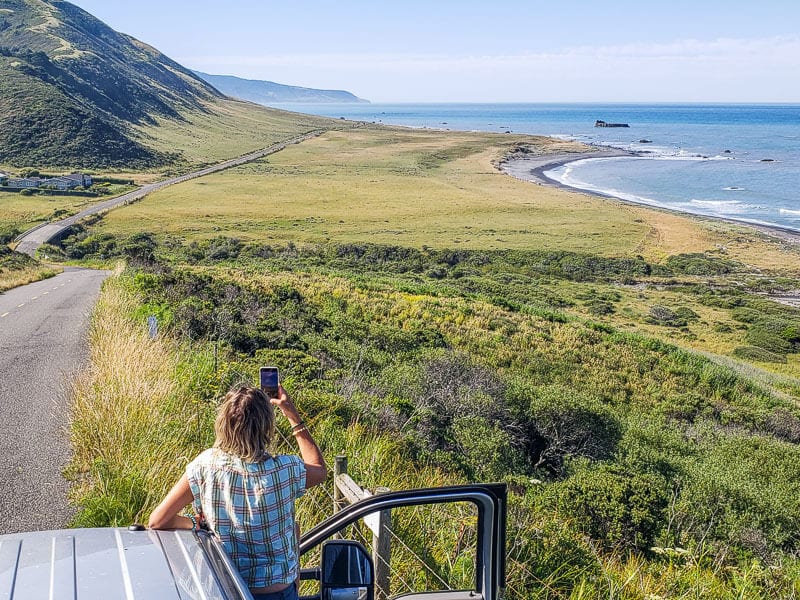 woman hangin gout of car taking photo of lost coast coastline in california